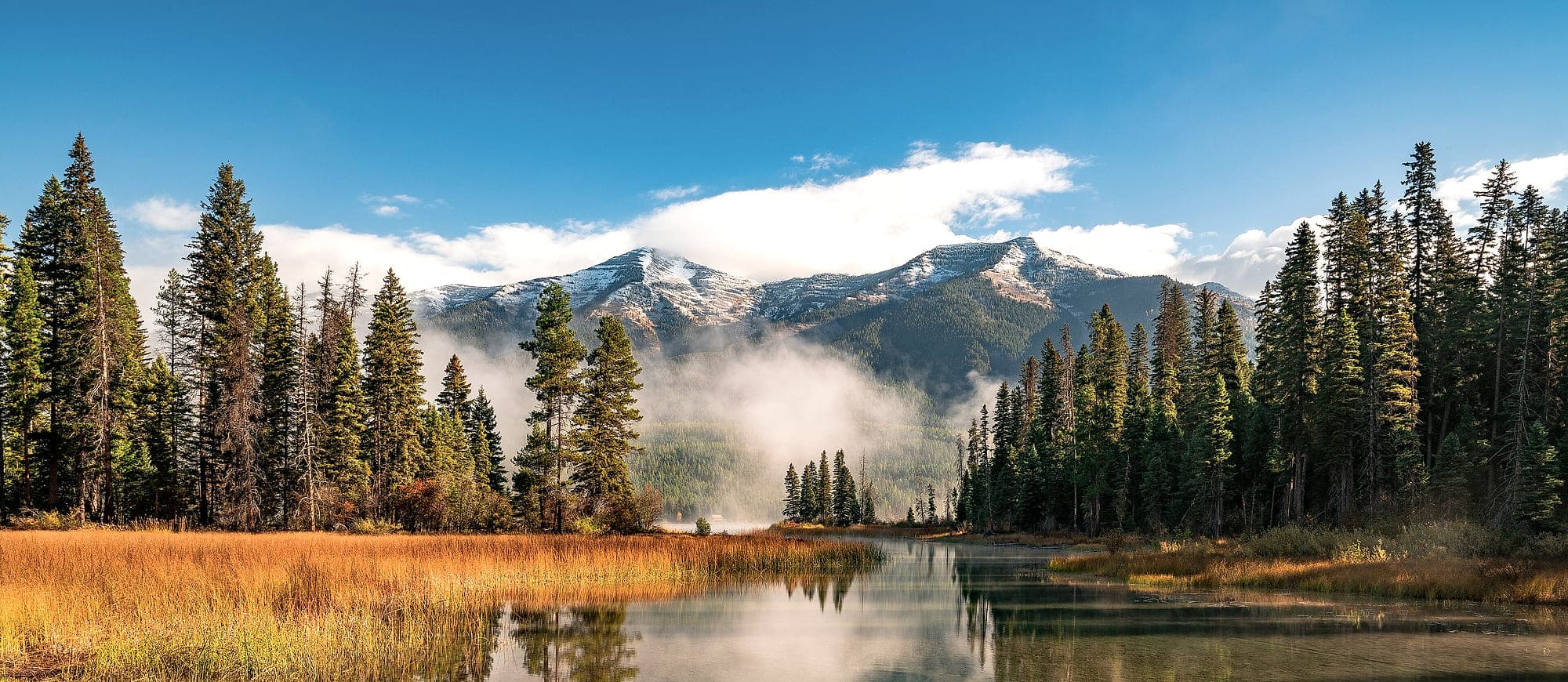 Fog lifting off a lake below snow-covered mountains, Flathead National Forest, Montana