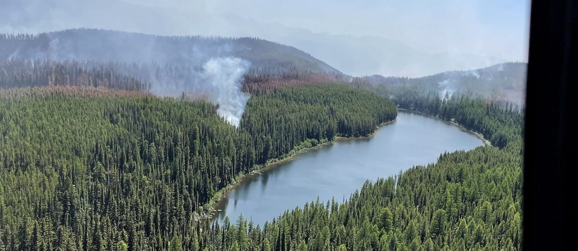 Smoke rising from a forested ridge above a river during the Colt Fire in western Montana